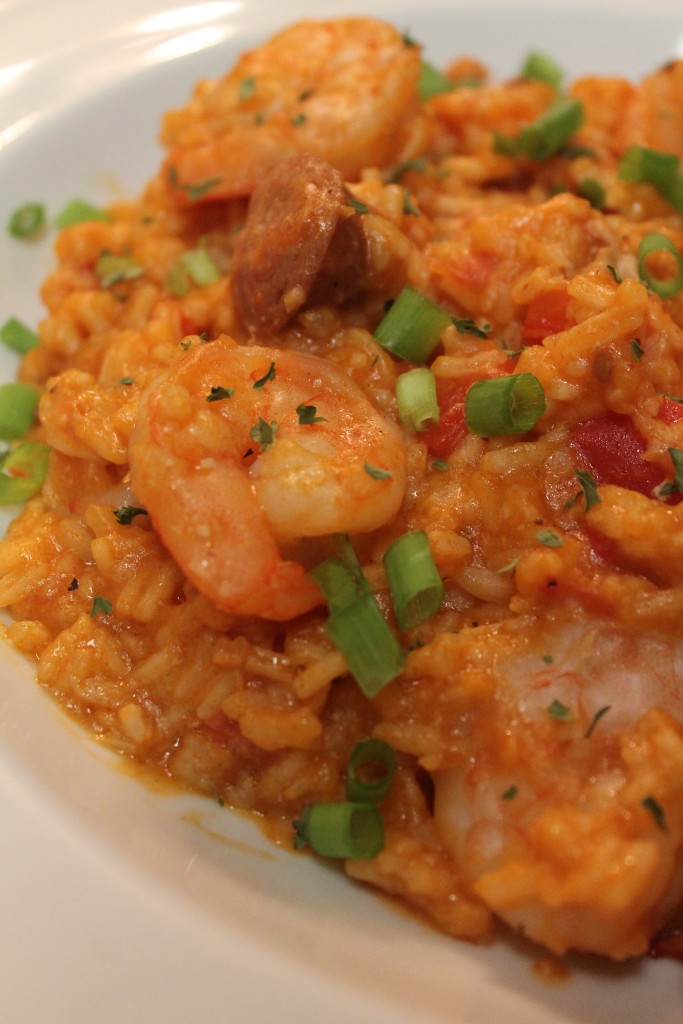 A close-up of jambalaya showcasing tender shrimp, Andouille sausage and chicken alongside seasoned rice all garnished with green onions.