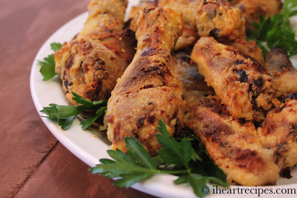 Pieces of extra crispy oven fried chicken drumsticks are stacked on a plate, garnished with fresh parsley leaves.