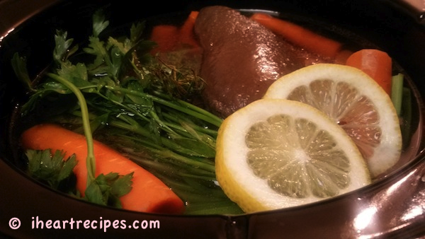 Frozen chicken stock, chopped veggies and herbs along with lemon slices are ready to simmer in a slow cooker. 
