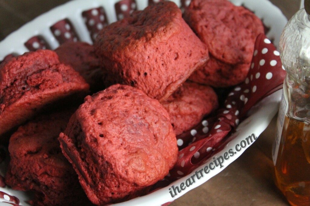 A white serving dish woven with red ribbon holds a pile of homemade, from-scratch Red Velvet Biscuits.