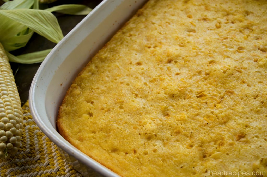 A casserole dish filled with a freshly baked corn pudding casserole. The corn pudding has a crisp surface with golden-brown edges, sprinkled with kernels of corn.