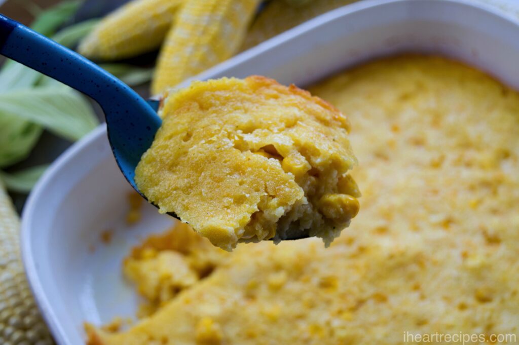 A scoop of corn pudding from a large casserole dish. Corn pudding is a sweet and creamy casserole made with creamed corn and Jiffy cornbread mix.