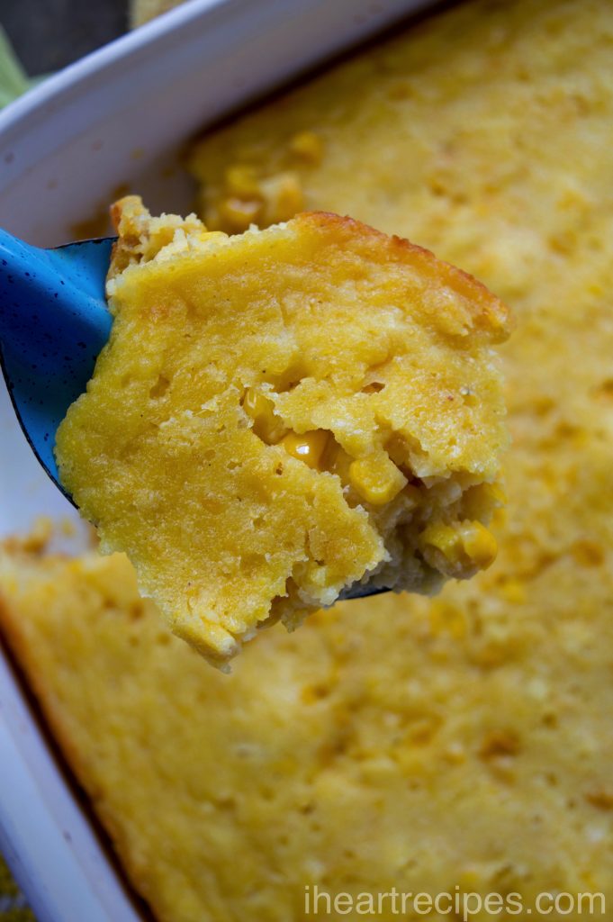 A large spoonful of creamy corn pudding scooped from a white casserole dish.