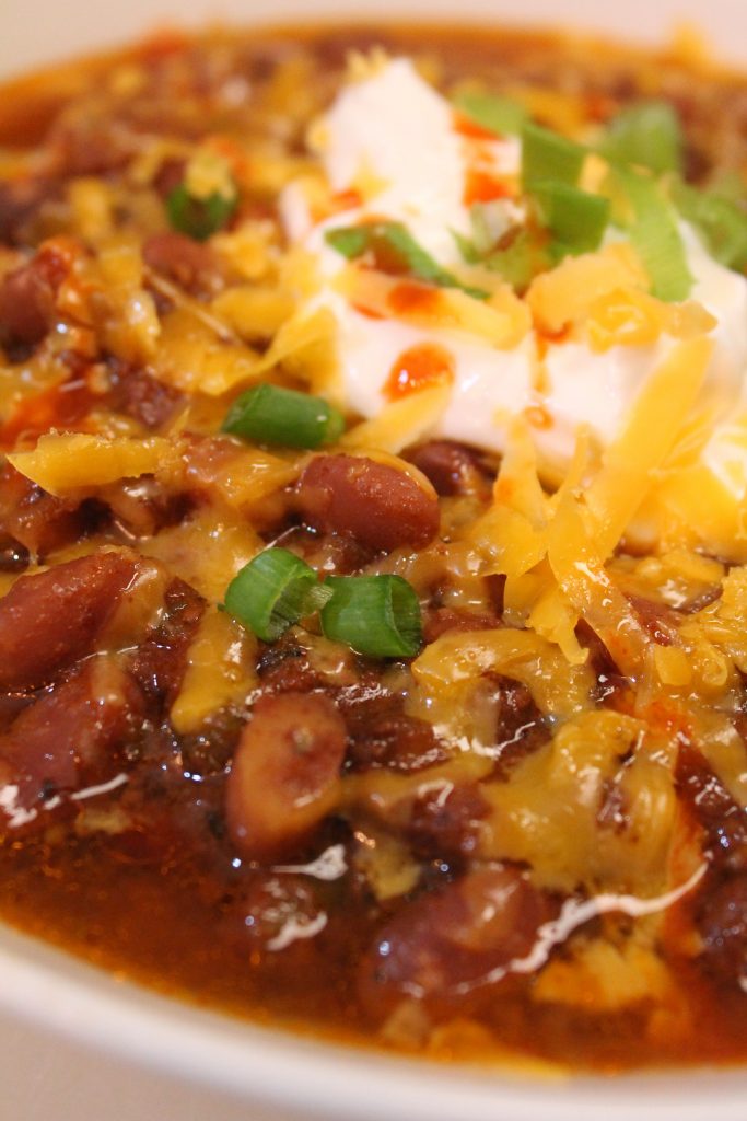 A hearty bowl of slow cooker beef chili with beans topped with cheese, sour cream, and green onions.