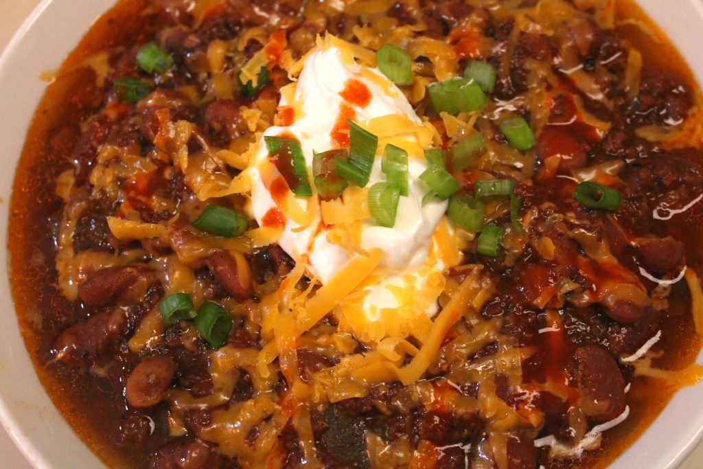 A large bowl of easy slow cooker chili topped with sour cream and shredded cheese.