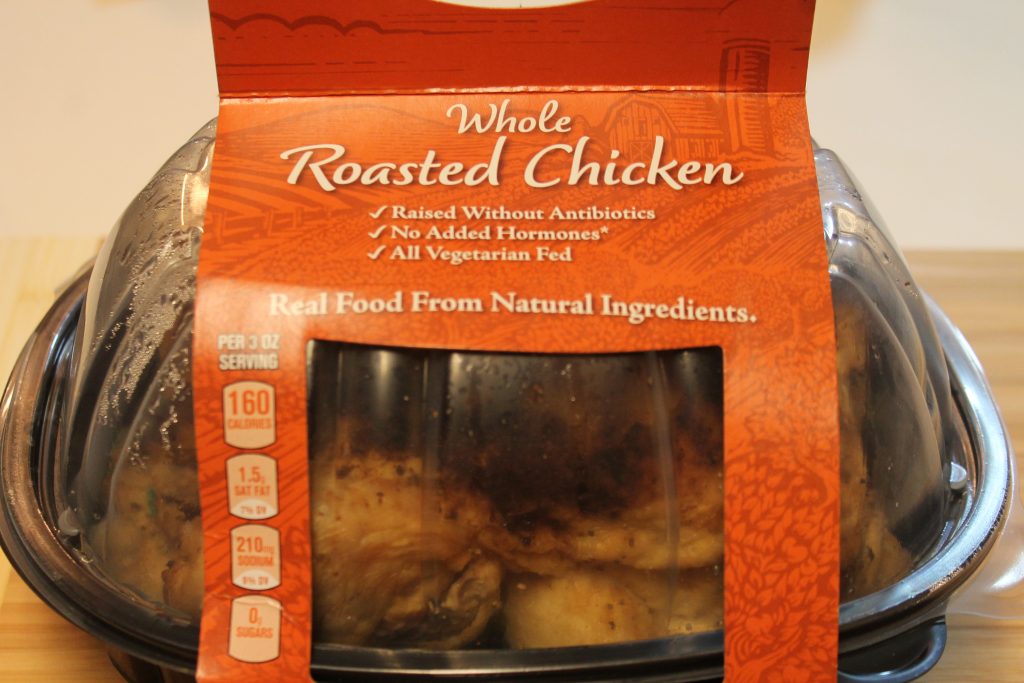 A rotisserie chicken in a clear and black plastic container wrapped in a red Safeway label.