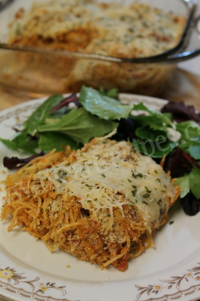 A serving of tender and savory chicken parmesan casserole with a bright green side salad served on white and floral china. A casserole dish is visible in the background. 