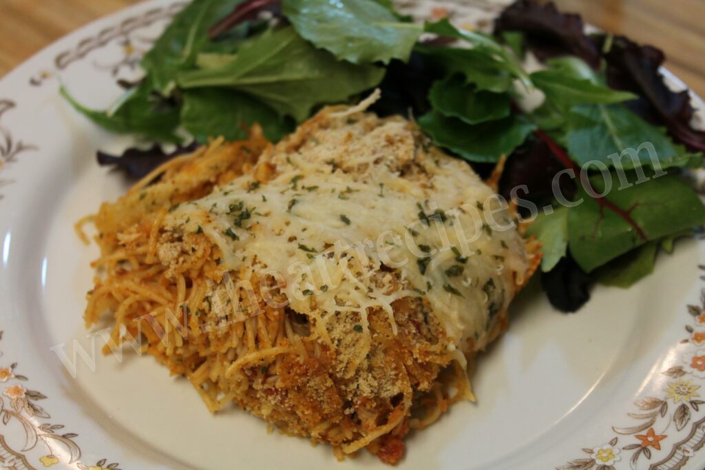 A serving of cheesy and hearty chicken parmesan casserole along with a bright green side salad on white and floral china. 