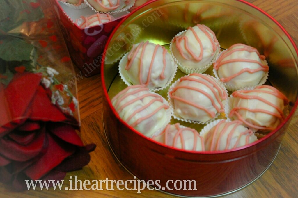 Strawberries and Cream Cake Truffles arranged in a single layer in a red tin can next to a red rose.