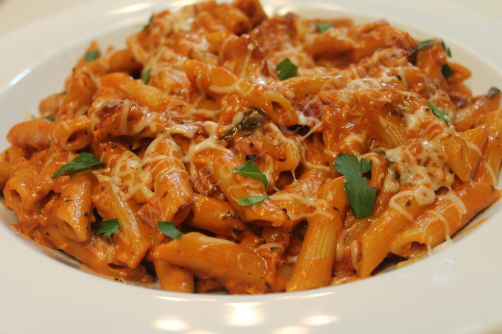 A white pasta bowl filled with tender Penne pasta drenched in creamy Homemade Vodka Sauce and garnished with fresh parsley leaves. 