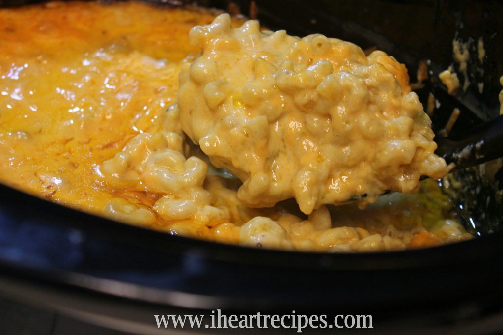 A heaping spoonful of creamy slow cooker macaroni and cheese is scooped out of a black Crockpot. 