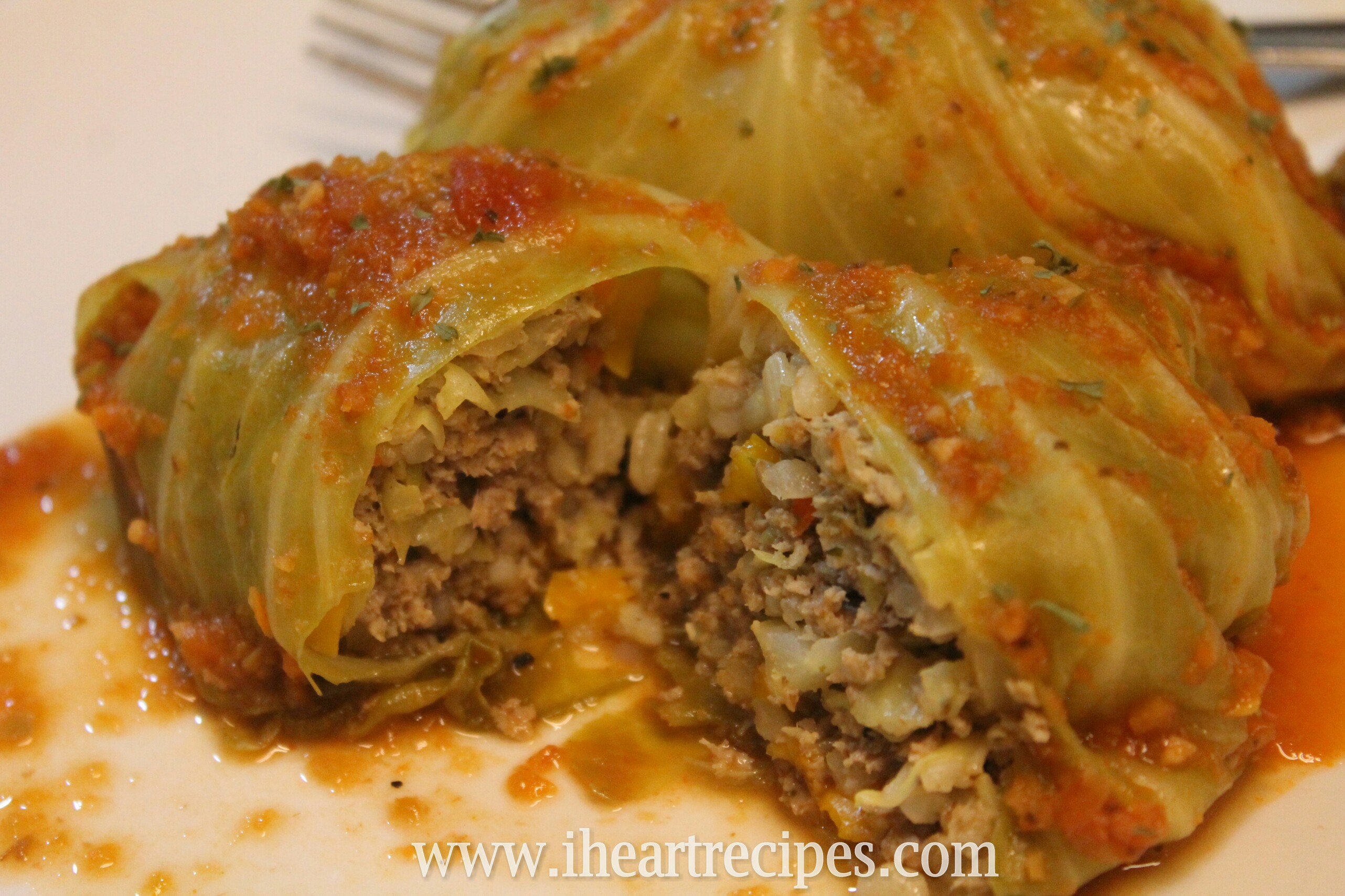 Two stuffed cabbage rolls covered in tomato sauce sit on a white plate. One cabbage roll is cut open, revealing a filling of ground turkey, rice, onions, and peppers.