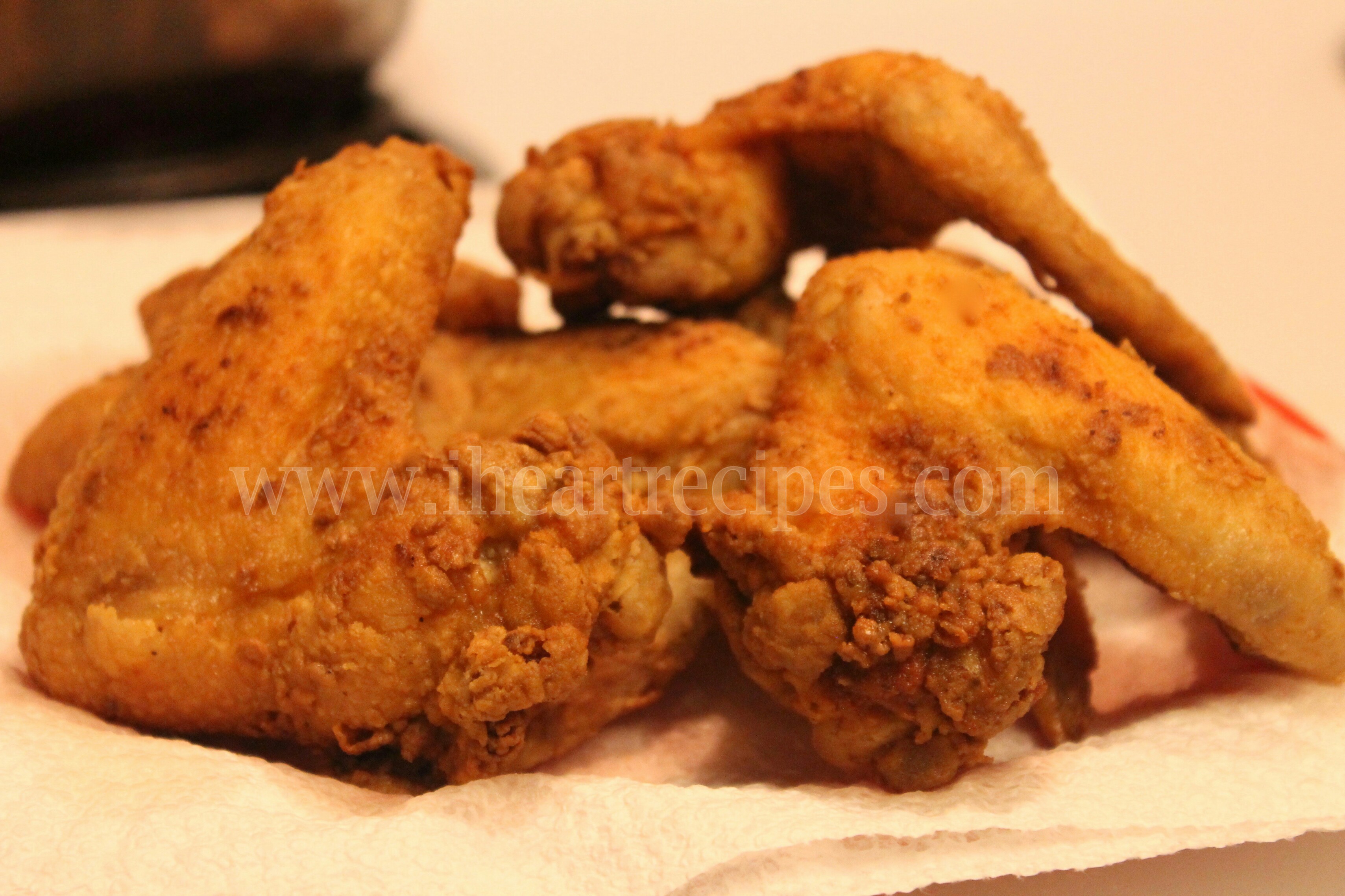 Several freshly fried chicken wings are stacked on paper towels. The wings are covered in a crispy golden-brown coating.