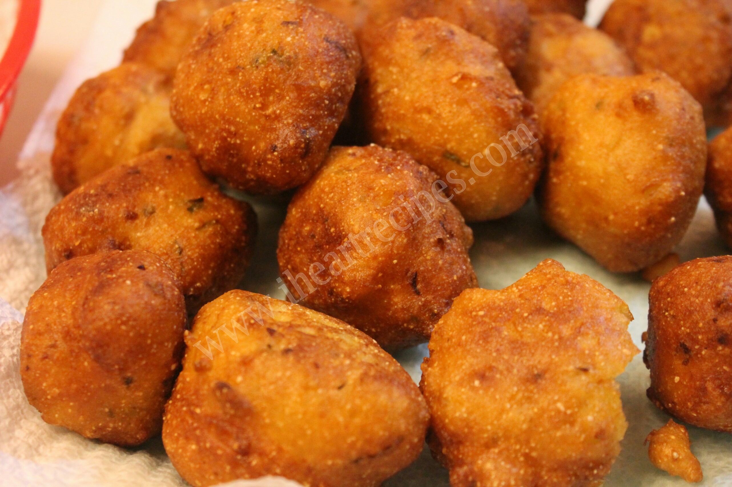 A close-up image of golden-brown deep-fried hush puppies sitting on a paper towel-lined plate.