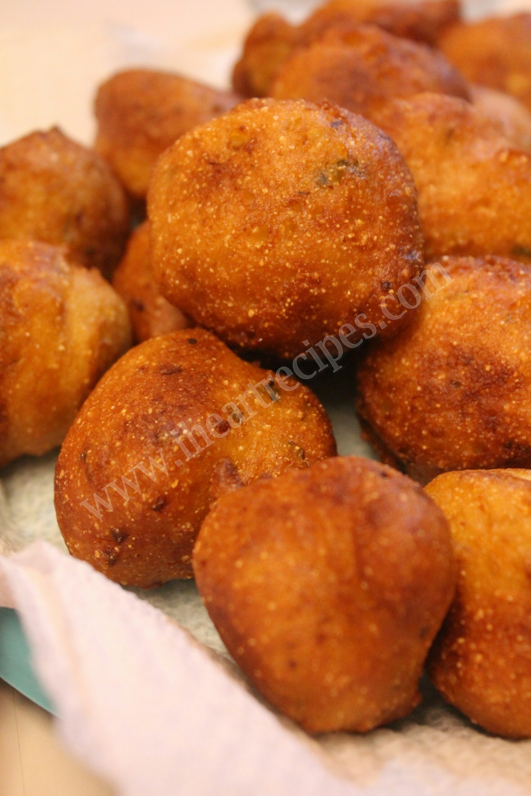 Freshly fried Southern hush puppies rest on a paper towel. The exterior is a crisp golden brown, with small specs of cornmeal and onions in the batter.
