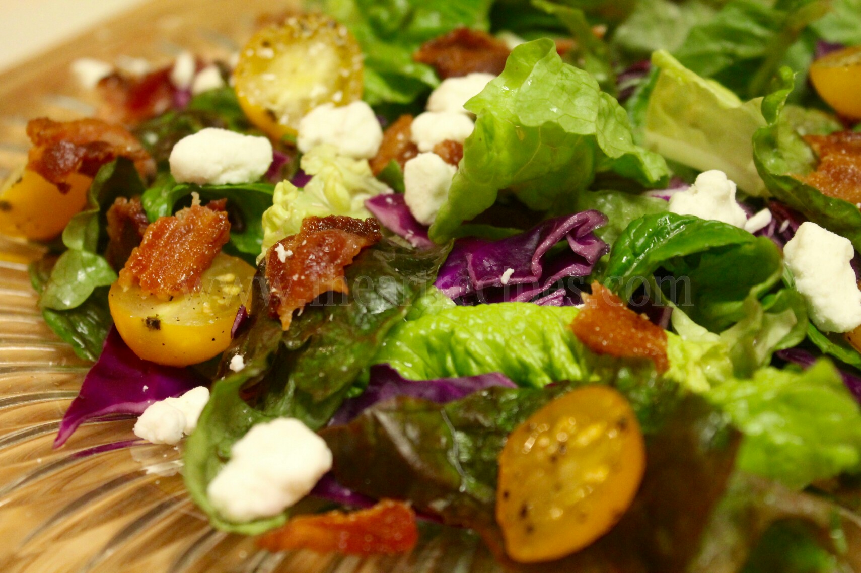 Colorful bacon and goat cheese spring salad served in a decorative peach glass salad bowl. 