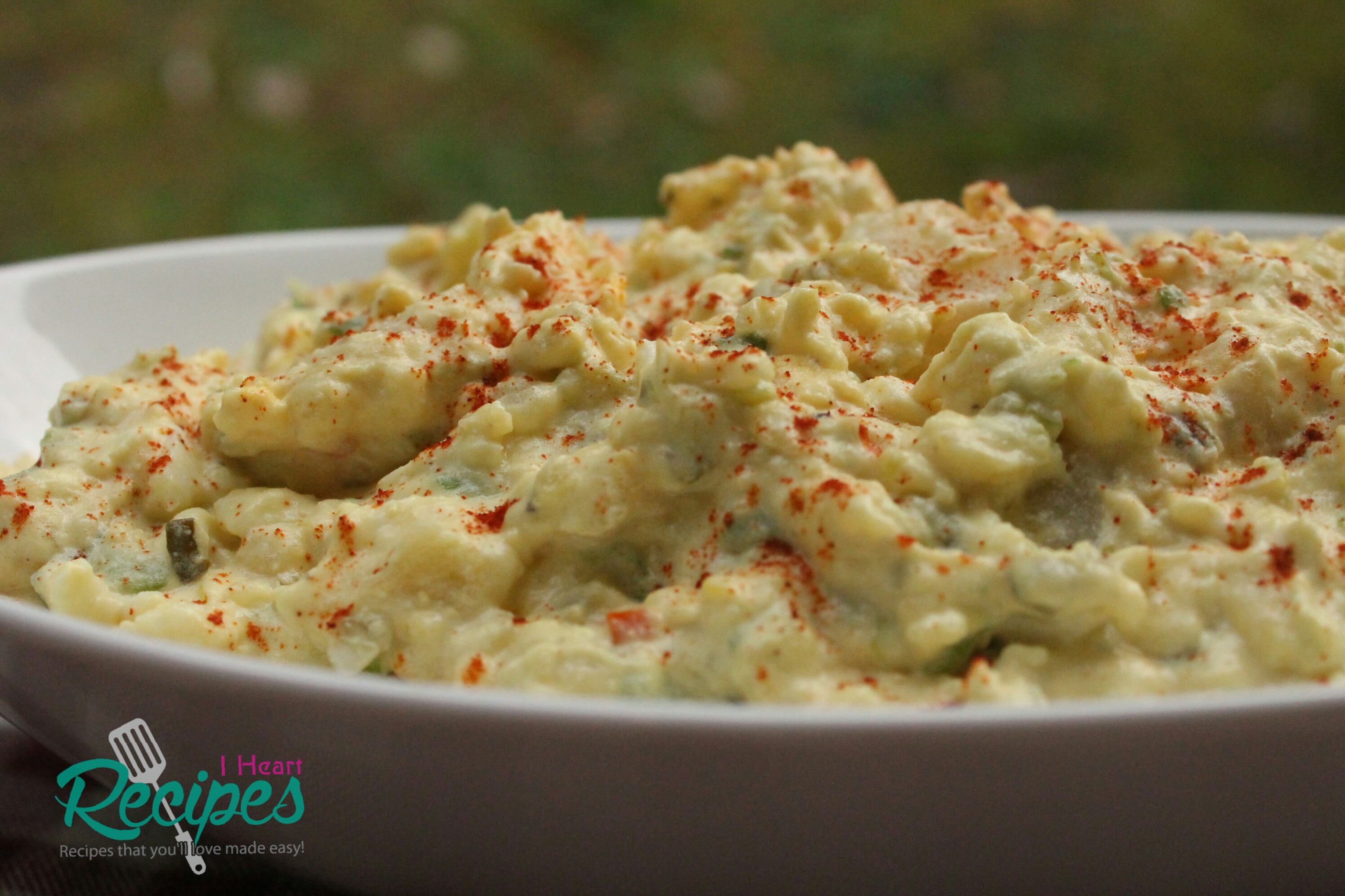 A side-angled image of a dish of Southern-style potato salad—a creamy salad of potatoes, vegetables, and dressing garnished with paprika.