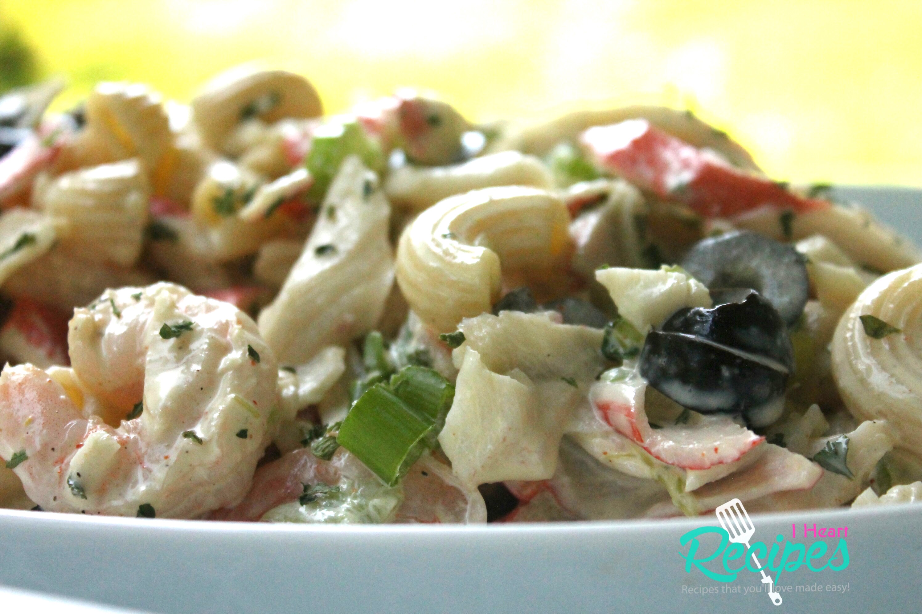 A side-angle view of a large bowl of seafood pasta salad, a creamy mix of crab meat, shrimp, veggies, and seasoning.