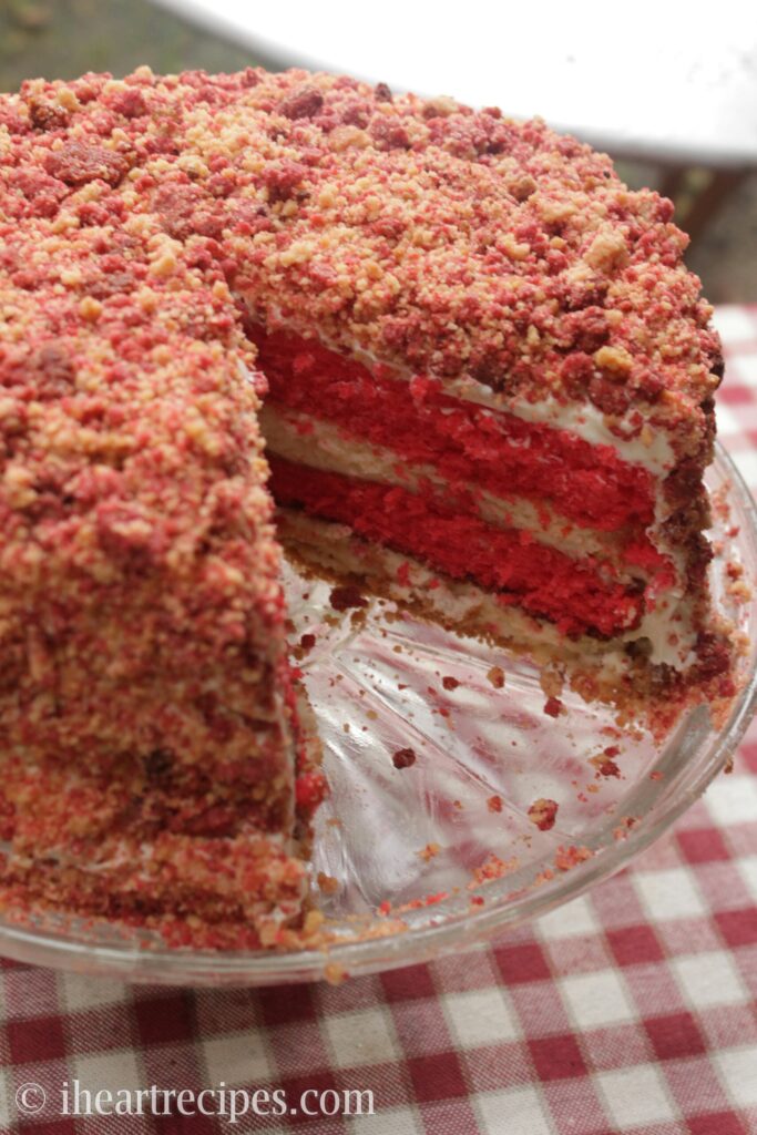A layered strawberry cake features layers of homemade cheesecake. A single slice is cut out, revealing the layers of cake and cheesecake inside.