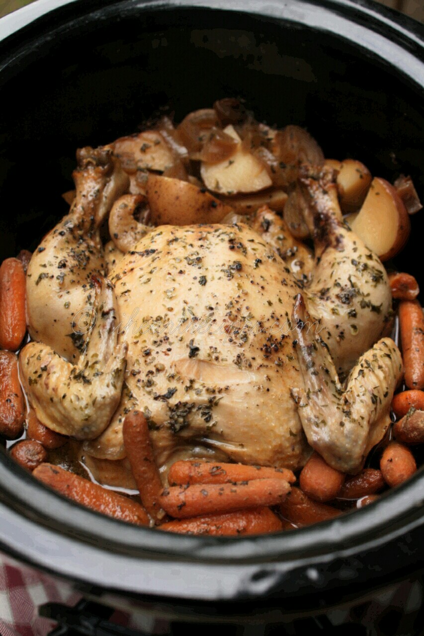 A simmering whole chicken with quartered red potatoes and baby carrots in a black slow cooker. This Slow Cooker Chicken Dinner is simple, savory and so delicious. 