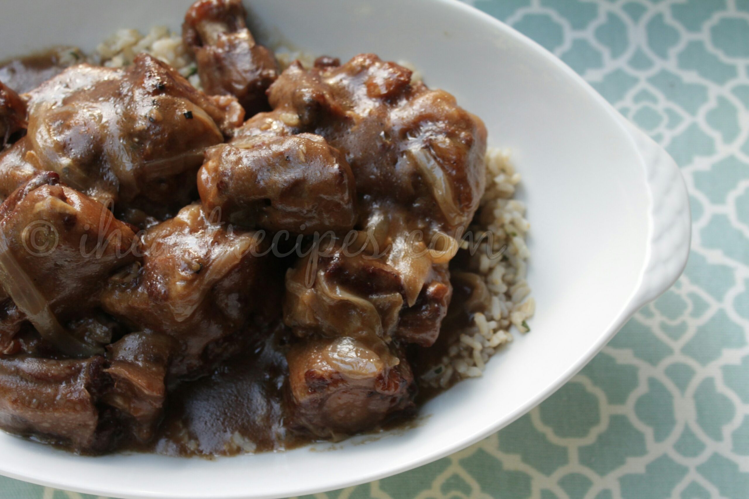 Slow-cooked smothered oxtails with gravy are served over a bed of rice in a white dish.