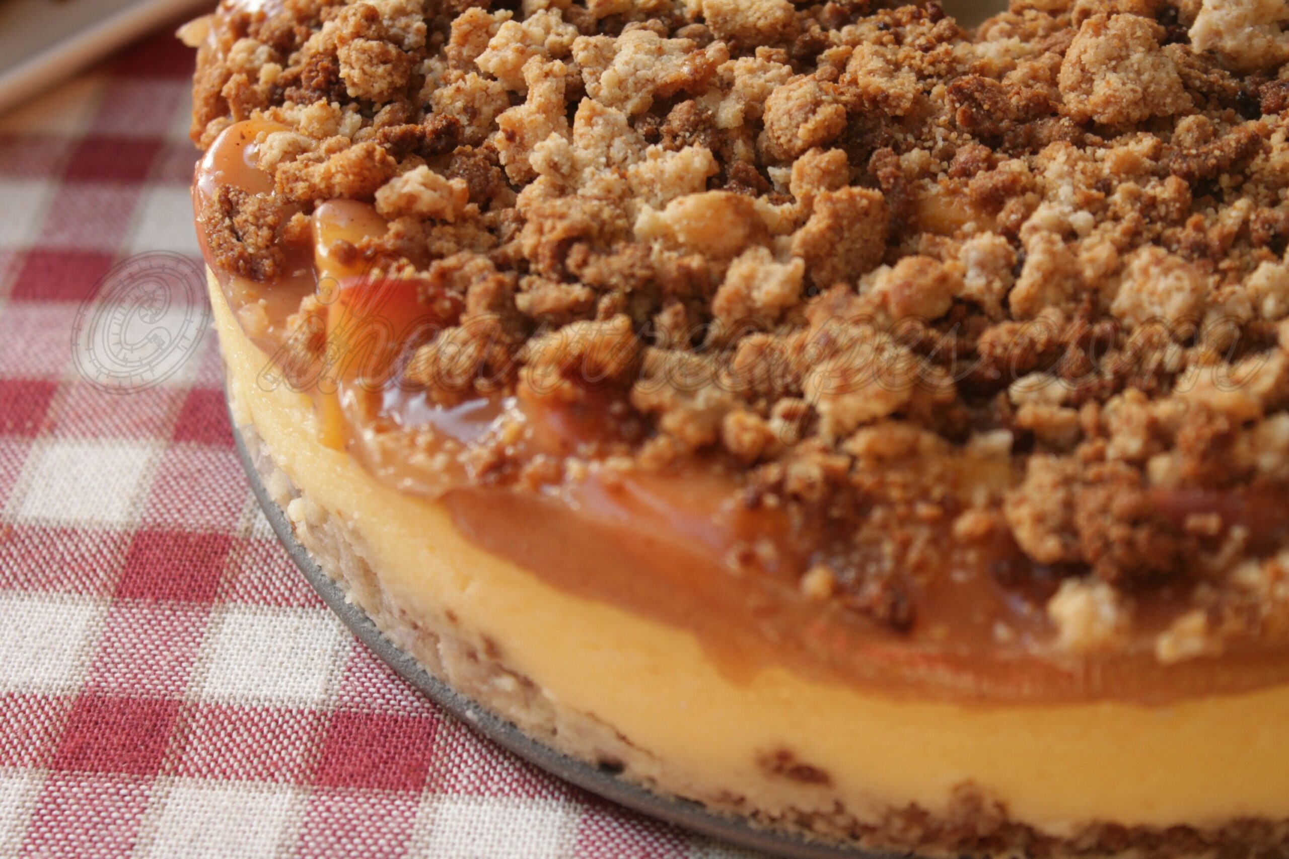 A close-up look at a homemade peach cobbler cheesecake with layers of fresh peach cobbler filling and creamy cheesecake, topped with a classic cobbler crumble topping.