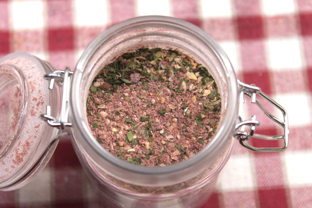Homemade taco seasoning fills a glass jar sitting on a red and white checked tablecloth.