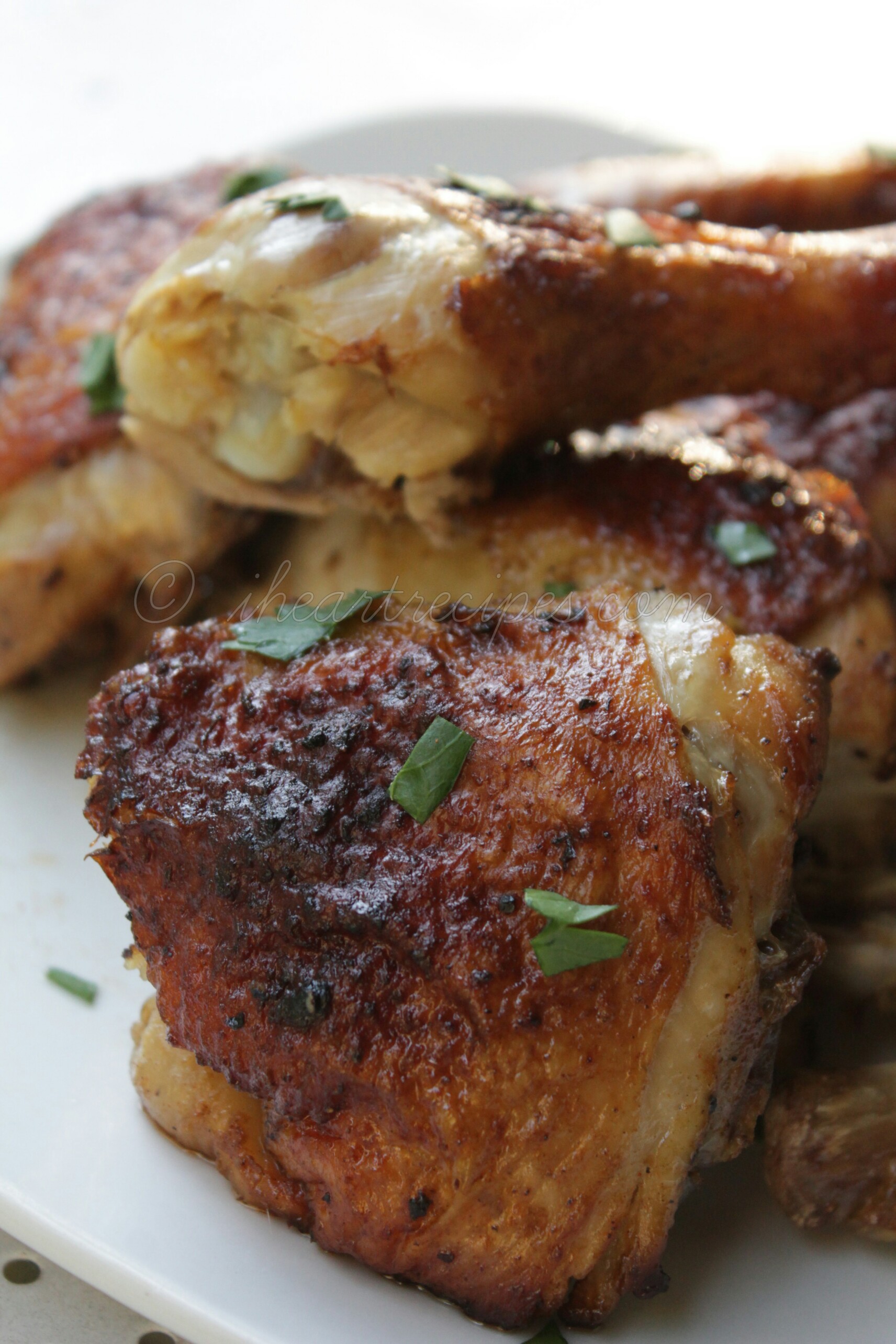 A close-up picture of a perfectly crispy roasted piece of chicken. The chicken is golden brown and dotted with fresh green herbs, presented on a clean white plate. 