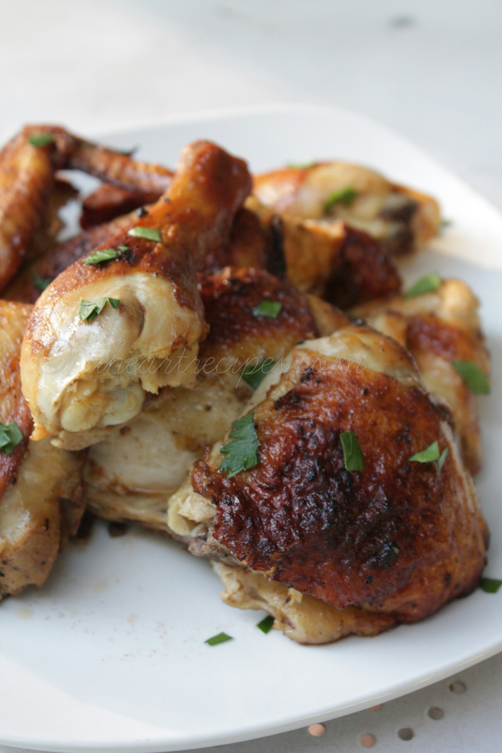 A square plate with oven roasted chicken pieces. The chicken is brown and crispy, sprinkled with fresh green herbs. 