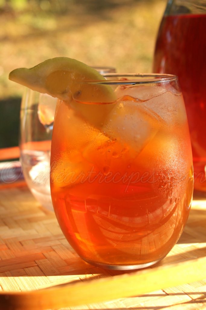 A close up of a glass tumbler filled with golden sweet tea and ice. A lemon wedge is resting on the rim. 