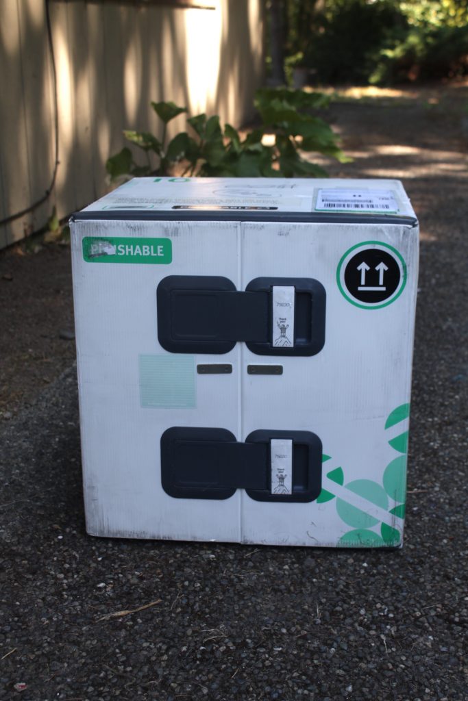A white, green and black box of Terra's Kitchen goodies sits on a blacktop driveway. Terra's Kitchen will deliver a box with a vessel to keep all of your ingredients cold and organized.