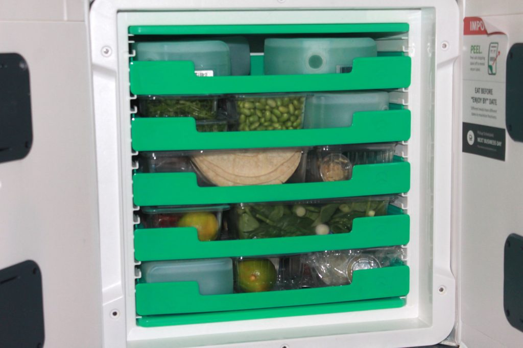 A mini refrigerator vessel with green shelves filled with fresh ingredients. 