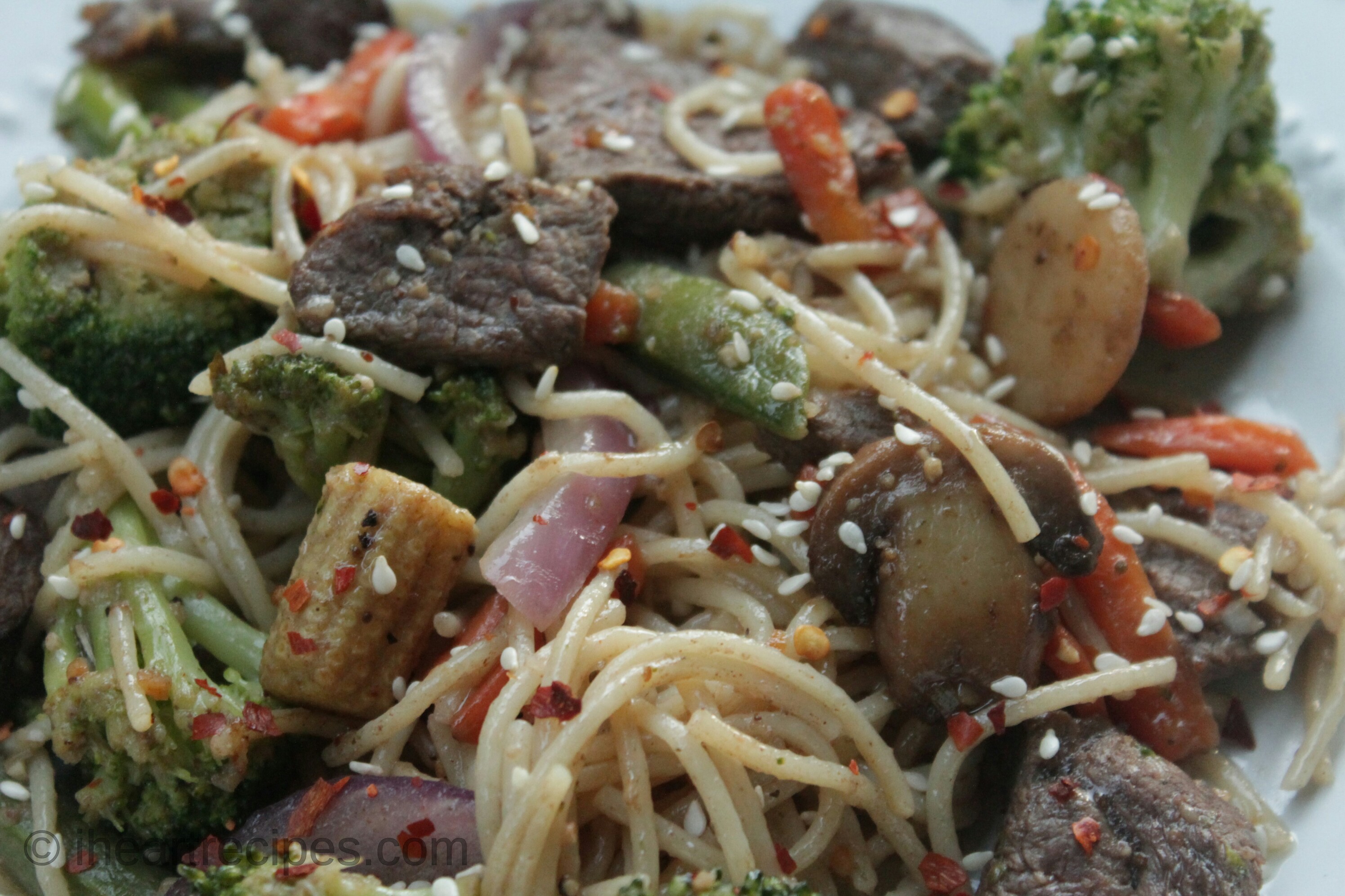 A close up image of an easy beef and vegetable stir fry with noodles served in a bowl. The stir fry contains broccoli, mini corn, peppers, and onions with marinated steak and spaghetti noodles.