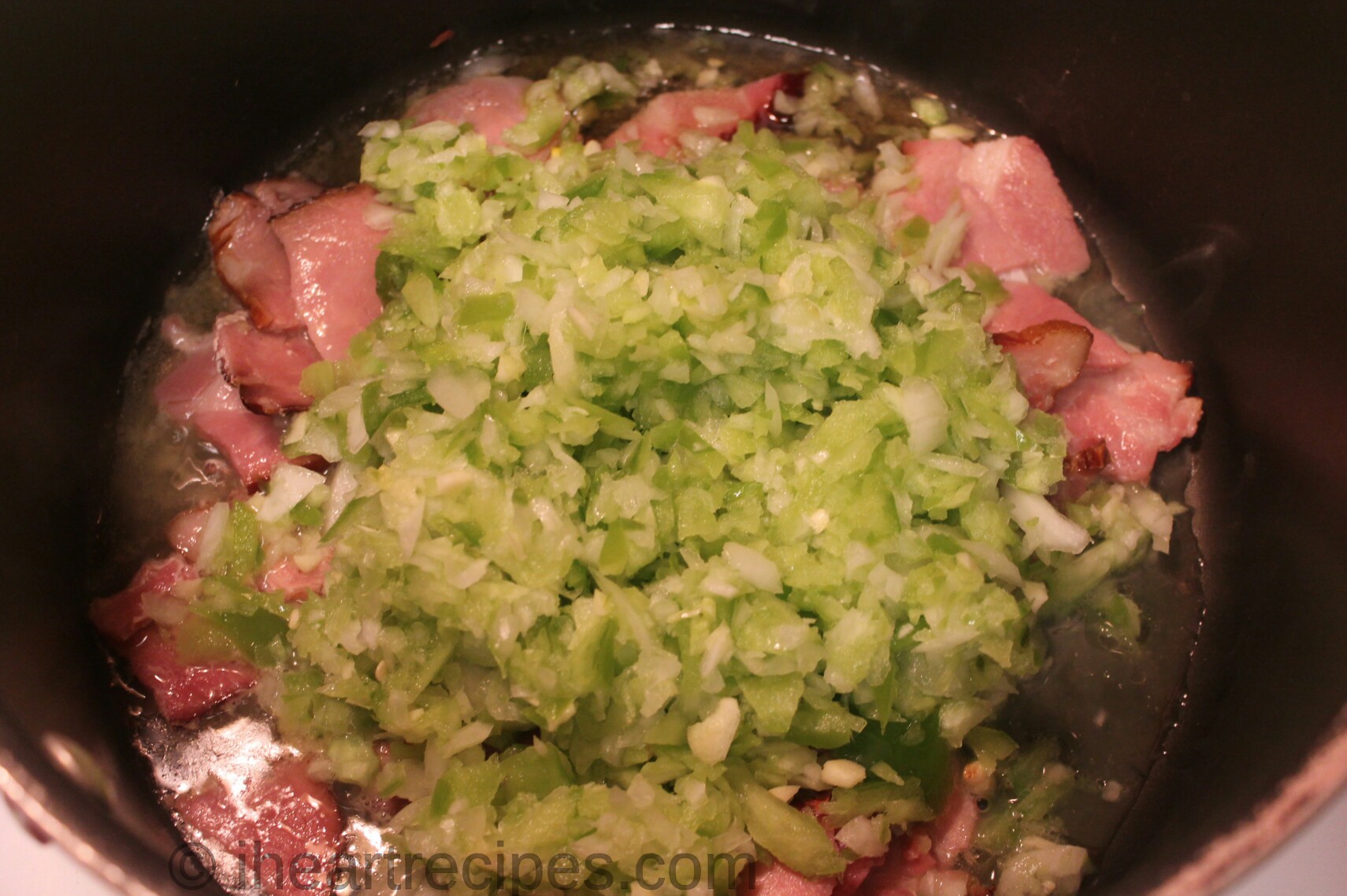 Chopped vegetables and bacon sauté on a large pot on the stovetop.