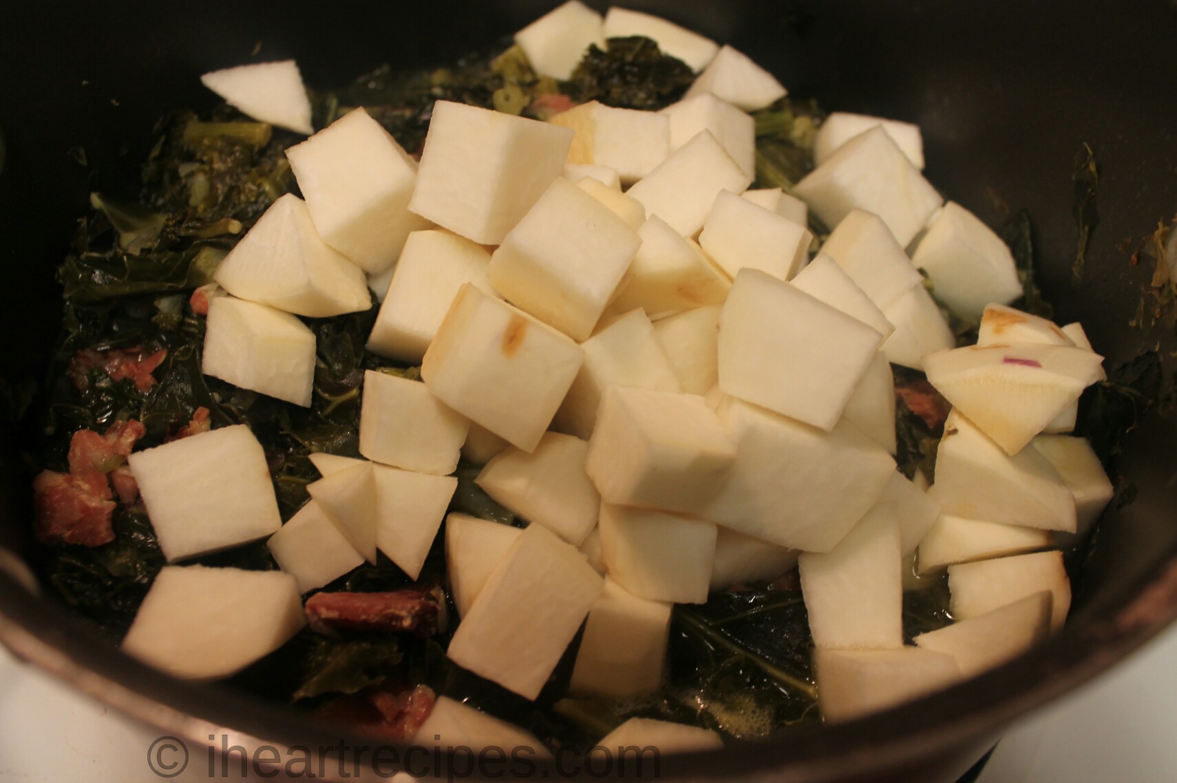 Cubed chopped-up raw turnips sit in a large pot of cooked Southern mixed greens.