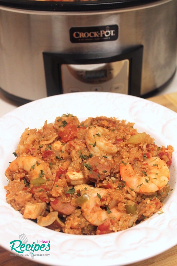 A shallow white bowl filled with Crock-Pot Quinoa Jambalaya next to a silver and black Crock-Pot. 