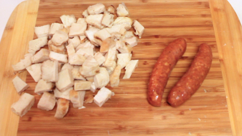 Cooked, chopped chicken and two links of andouille sausage on a wood cutting board. 