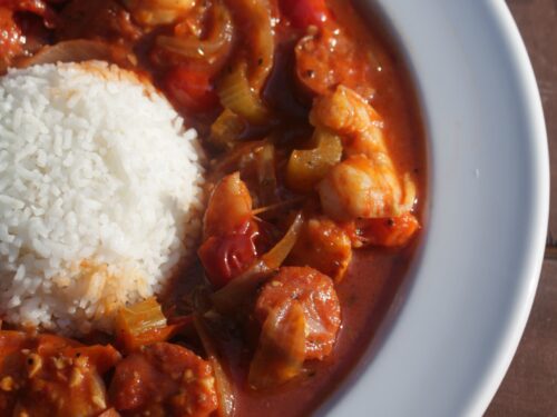 A close-up picture of shrimp and sausage creole served in a bowl around a mound of white rice.