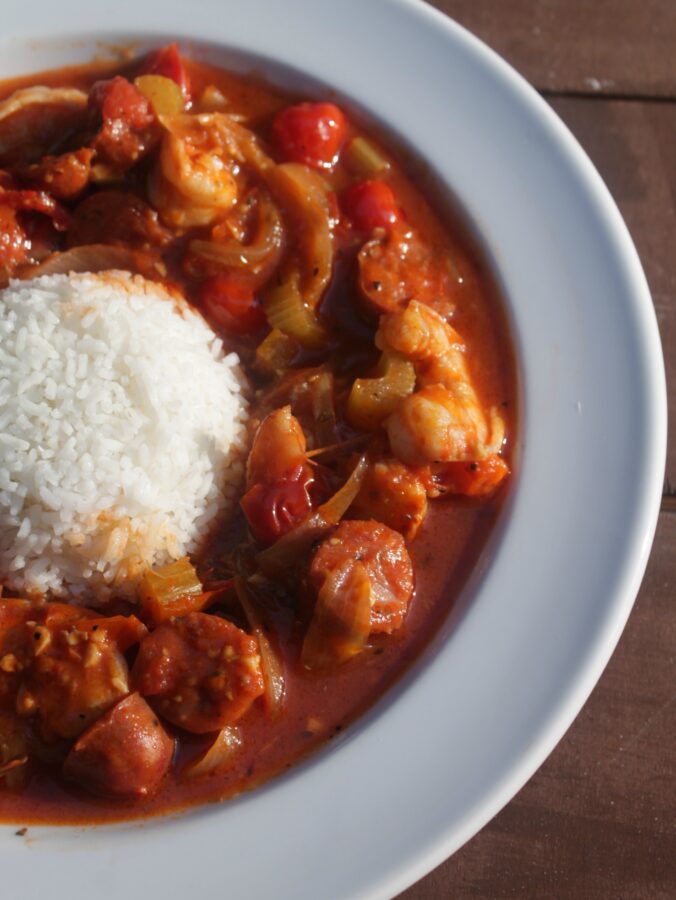 A close-up picture of shrimp and sausage creole served in a bowl around a mound of white rice.