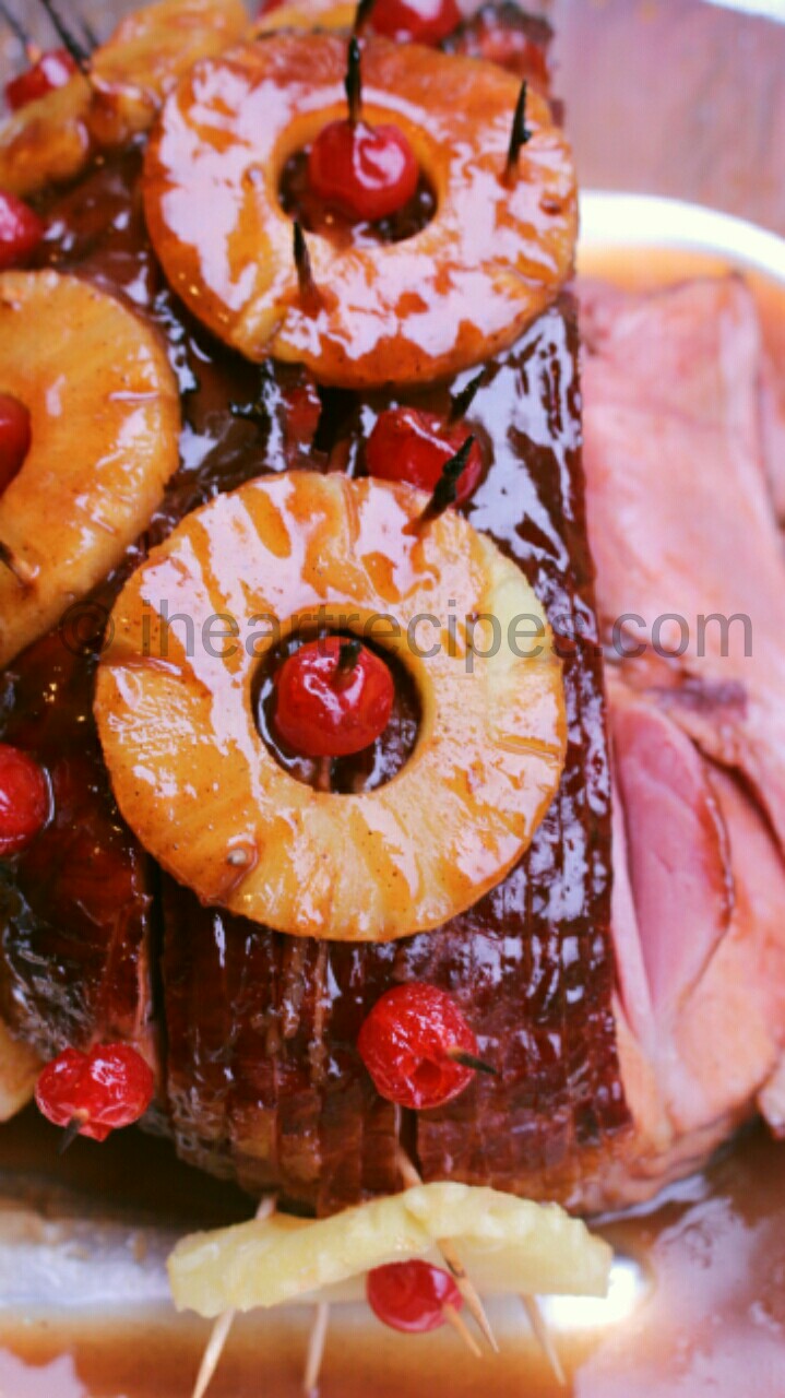 A close up image of a spiral ham decorated with pineapple rings and maraschino cherry slices. The ham is coated in a thick pineapple brown sugar glaze.