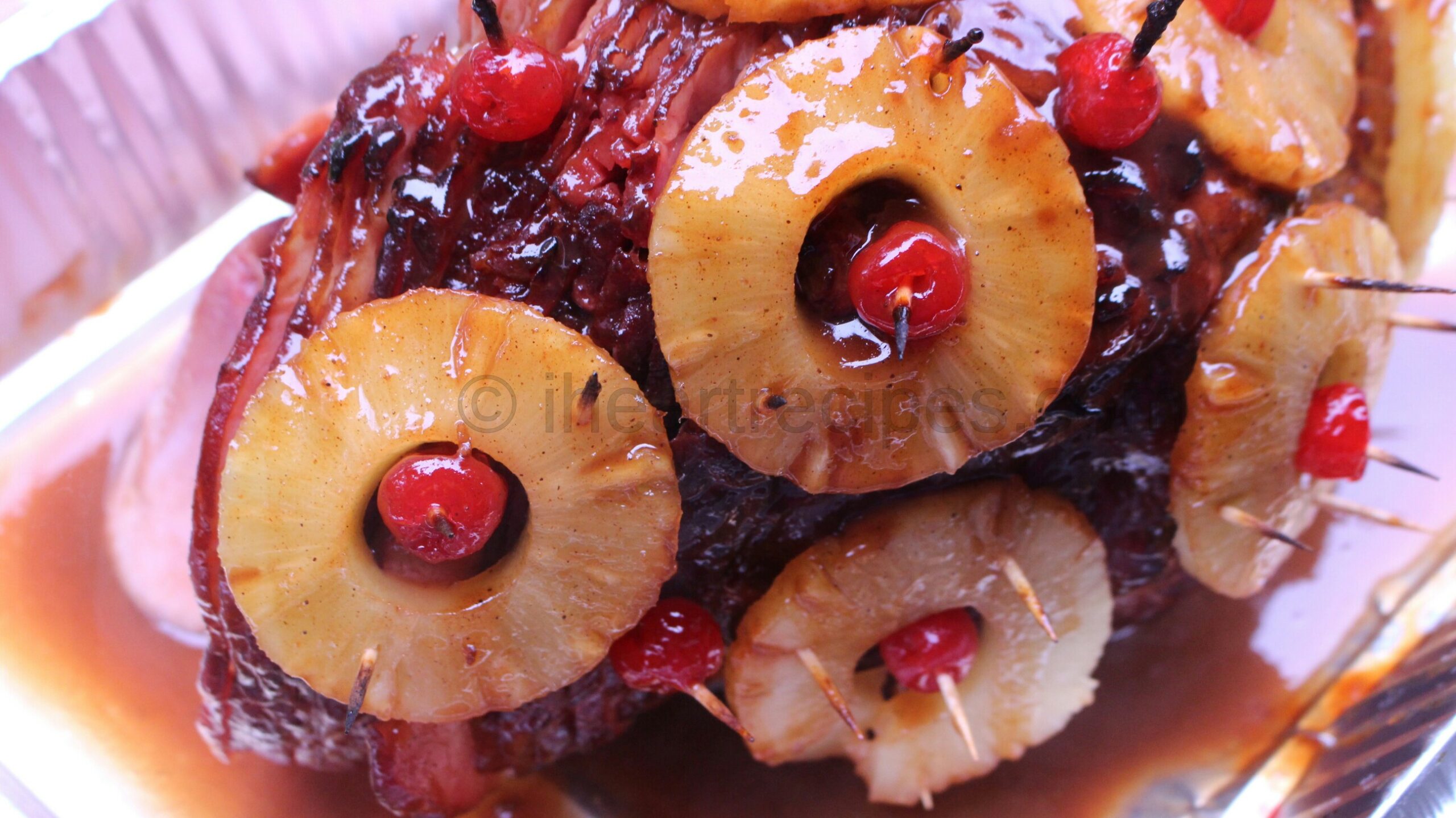A close up image of a baked spiral ham garnished with pineapple rings and cherries, glazed with a sweet pineapple brown sugar sauce.
