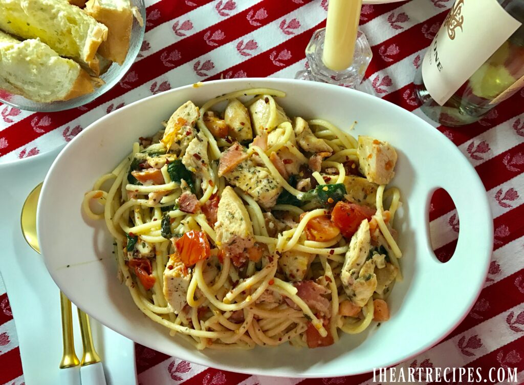 An overhead image of lemon chicken with tender bucatini pasta served in a simple white pasta bowl alongside white wine and crusty Italian bread.