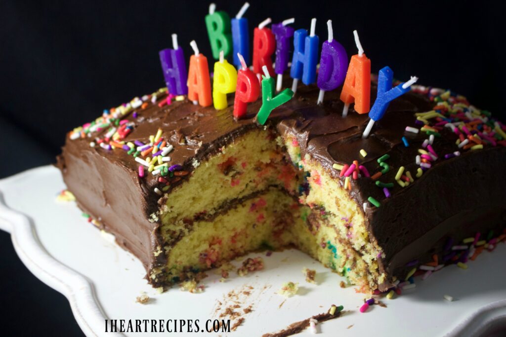 A moist, fluffy, double-layer birthday cake served on a scalloped white cake pedestal. 