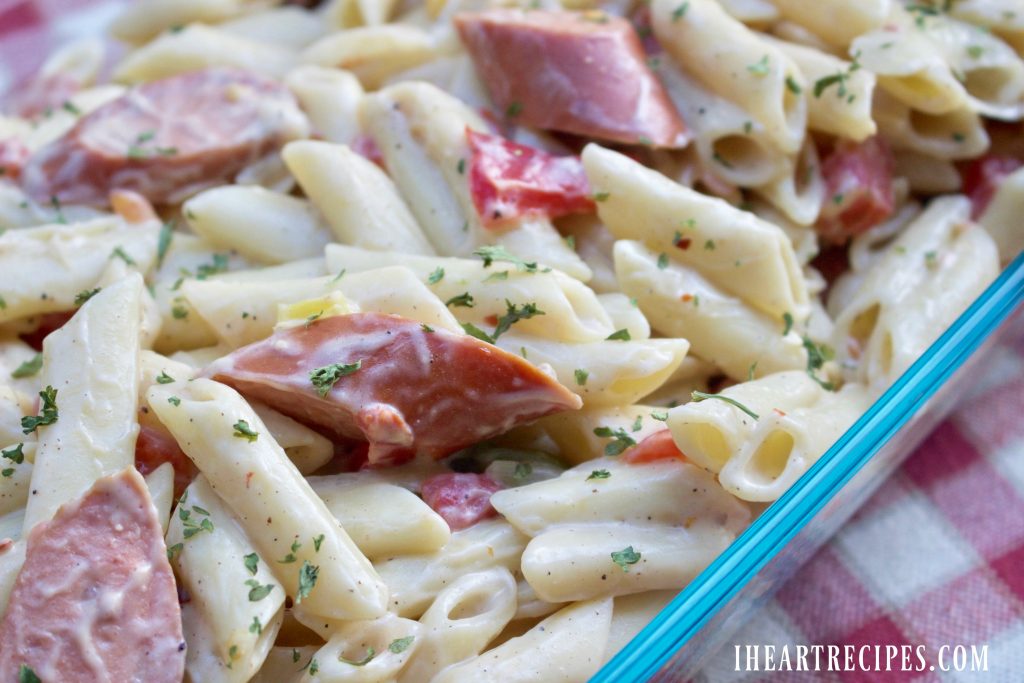 Savory and Creamy Jambalaya Pasta fills a glass baking dish set on a red and white checkered tablecloth. This recipe is made with Dollar Store ingredients for a budget-friendly meal.