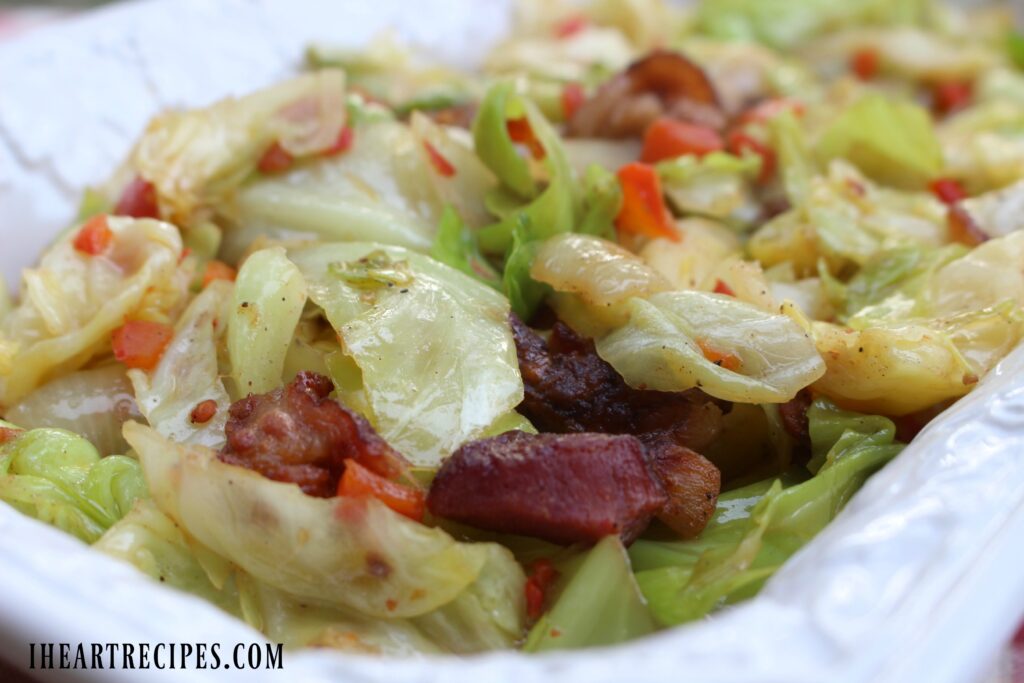 A close up of fried cabbage with chunks of tender meat served in a classic white serving dish. 