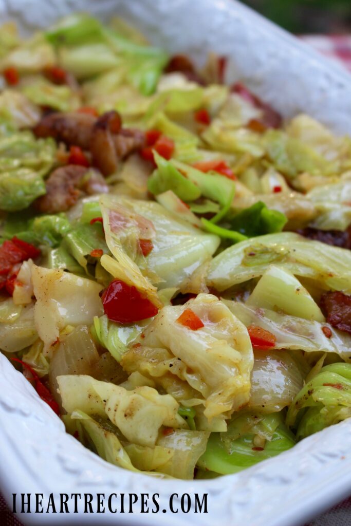 A close-up image of Southern fried cabbage with bacon, onions, and peppers served on a white platter.