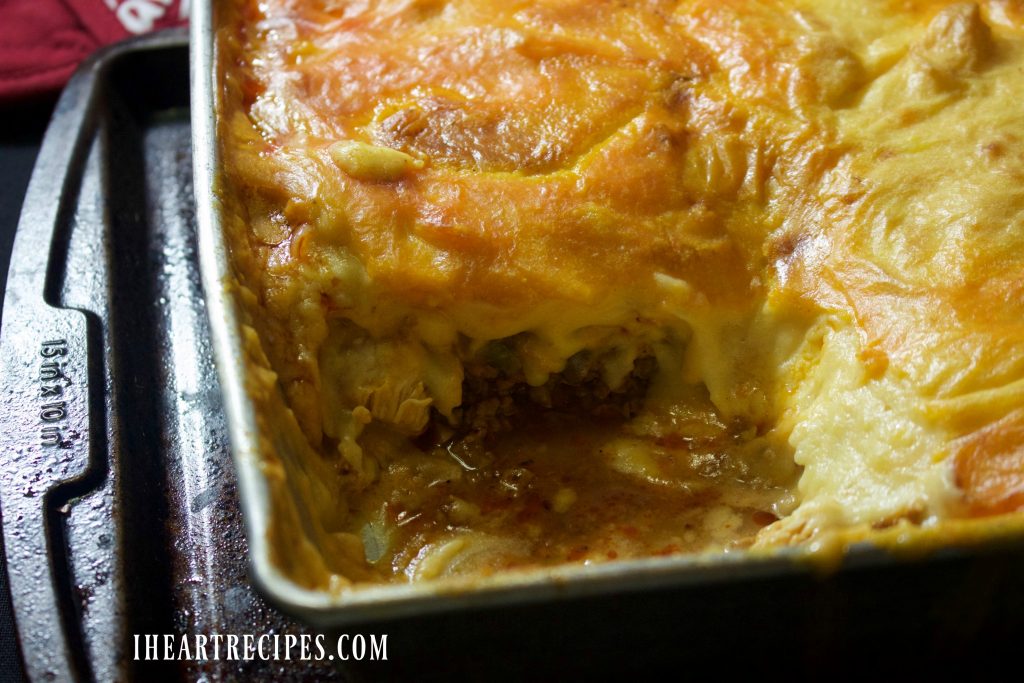 Savory filling topped with cheesy potatoes fill a silver baking dish. 