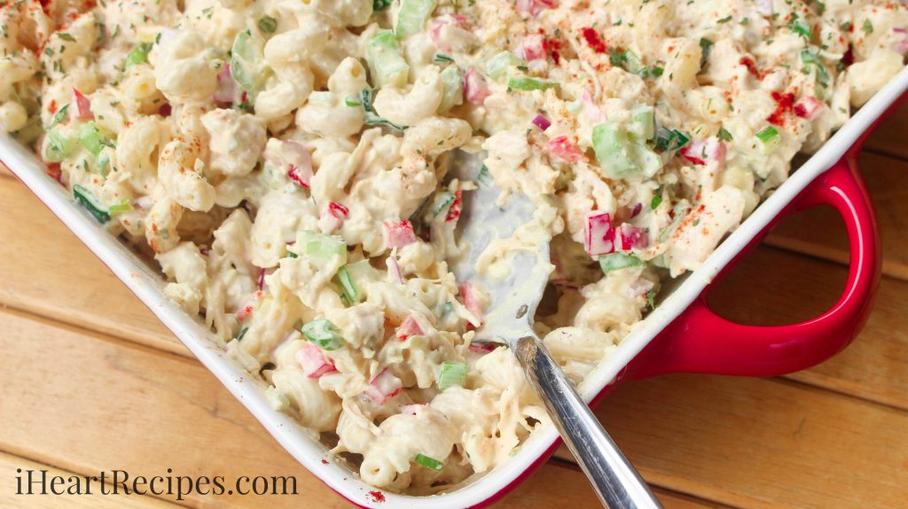 A white and red casserole dish is filled with a creamy chicken macaroni salad packed with chicken, pasta, and fresh veggies.