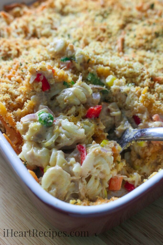 Creamy noodles and crisp veggies topped with a buttery and crunchy bread crumb topping being served from a red baking dish. 