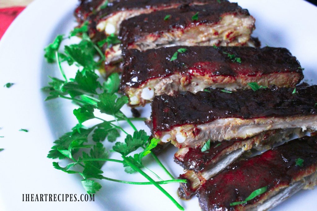 Tender pieces of ribs coated in a tangy BBQ sauce, garnished with fresh parsley, served on a white serving platter.